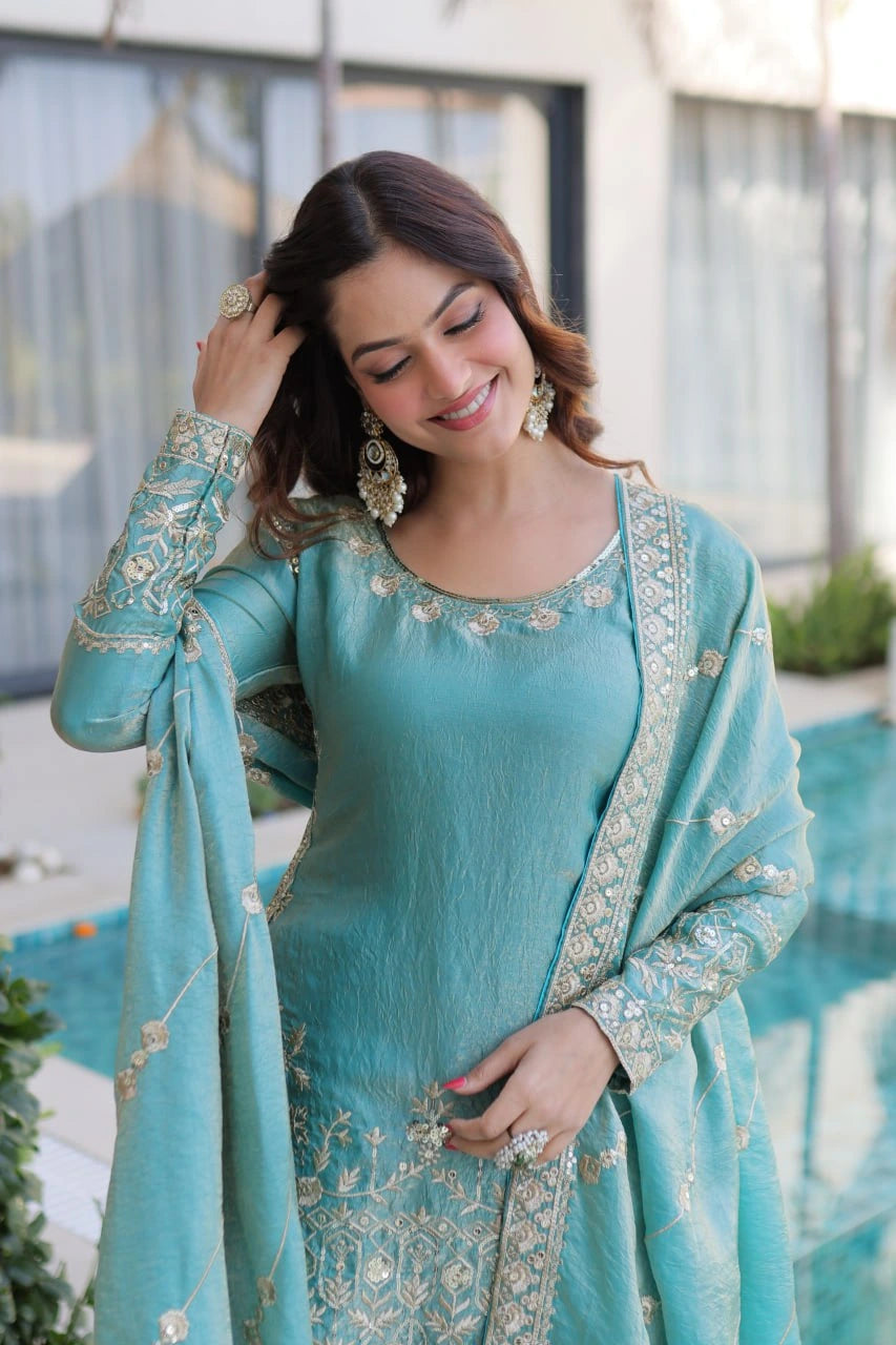 Woman in a light blue traditional outfit with embroidery, standing by a pool.