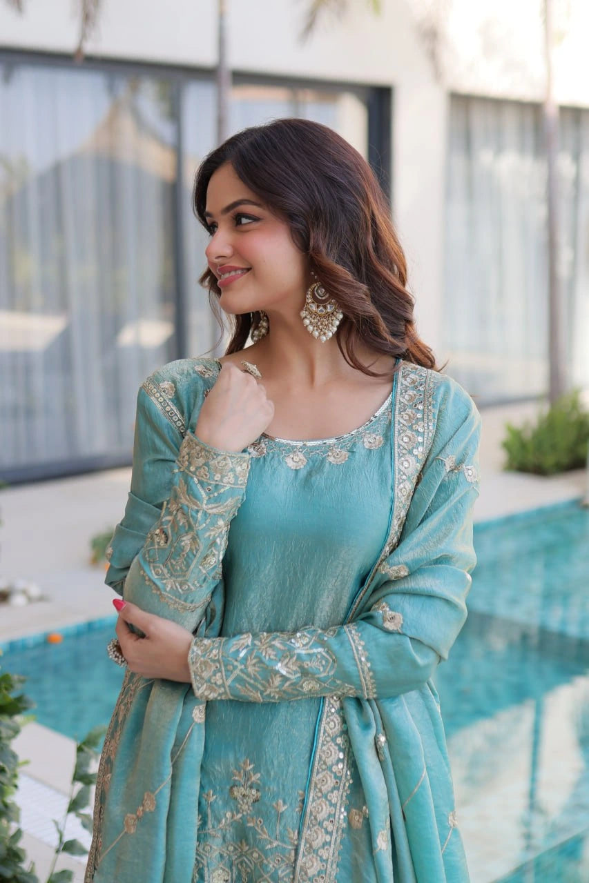 Woman in a teal traditional outfit with embroidery, standing by a pool.
