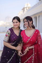 Two women in traditional sarees standing together outdoors with a building in the background.
