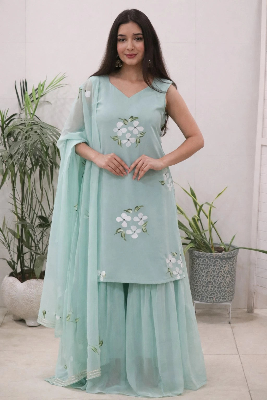 Woman wearing a light blue traditional outfit with floral embroidery in a home setting.