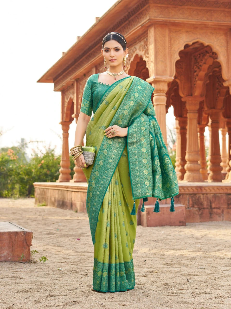 Woman in a green saree standing in front of an architectural structure.