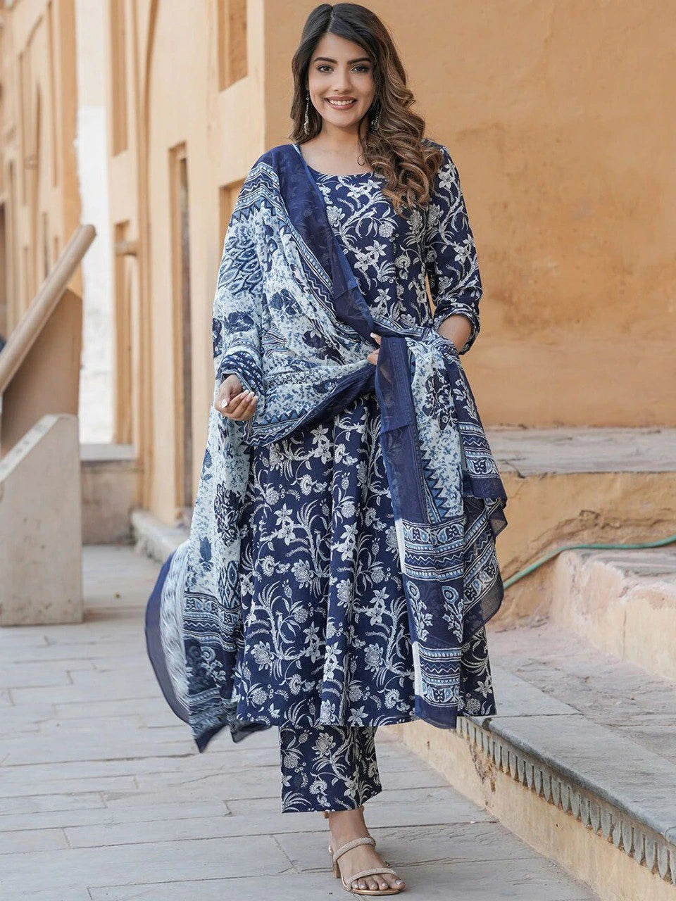 Woman wearing a blue and white patterned outfit standing in front of a beige wall.