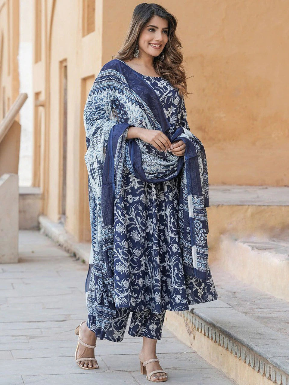 Woman wearing a blue and white patterned outfit standing on steps with a beige wall in the background