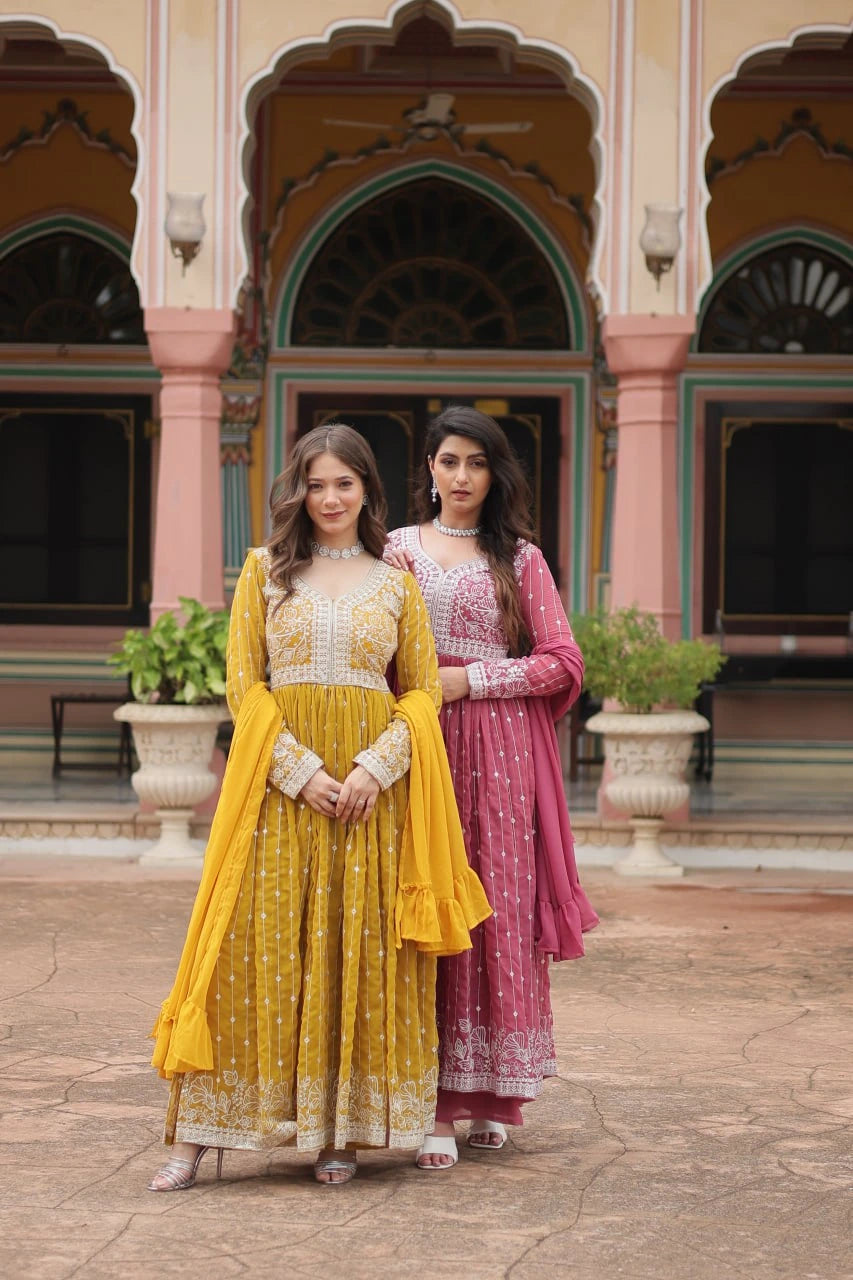 Two women in traditional yellow and pink dresses standing in front of a decorative building.