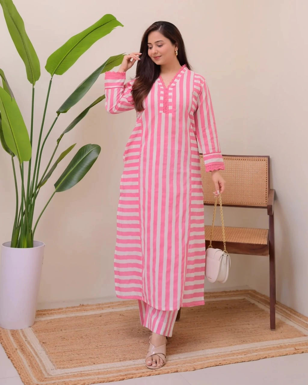 Woman in a pink and white striped outfit standing next to a plant indoors.