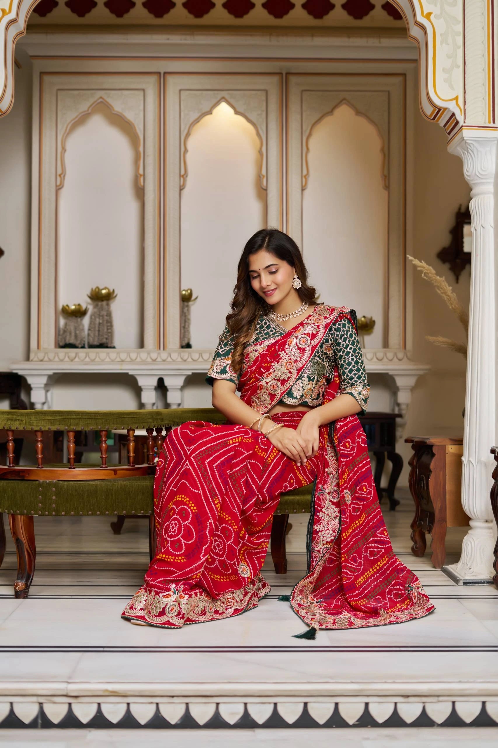 Woman in a traditional saree sitting in an ornate room.