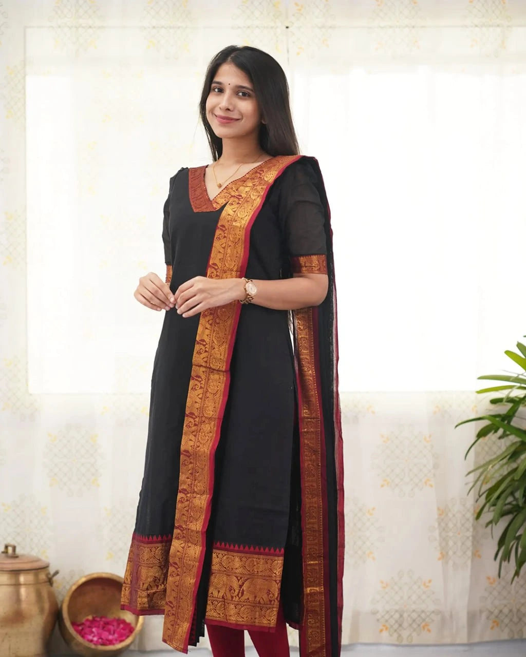 Woman wearing a black dress with orange and red border, standing against a light background.