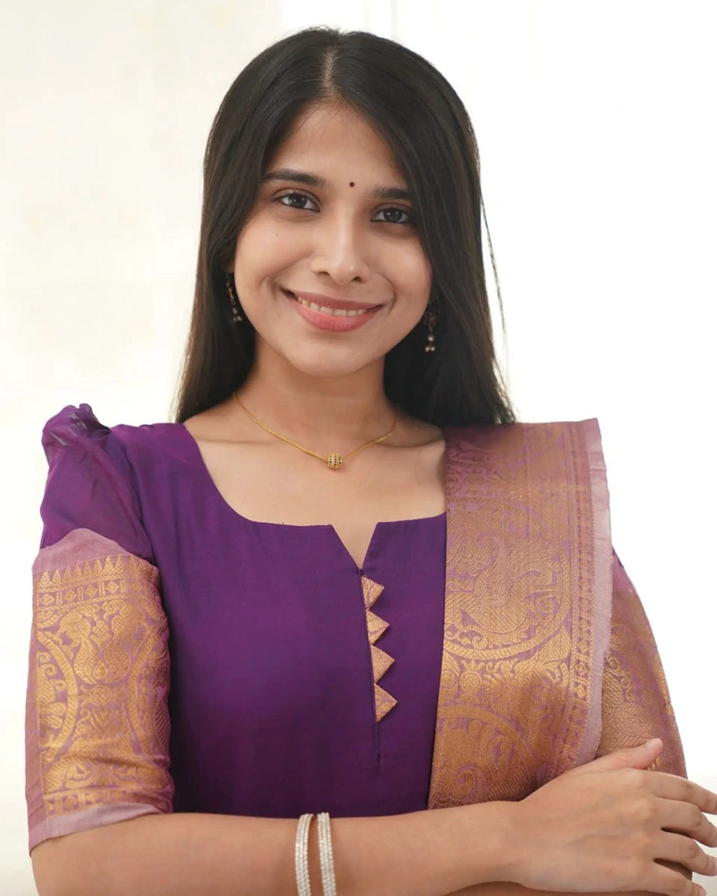 Woman wearing a purple blouse with a gold and purple saree on a white background