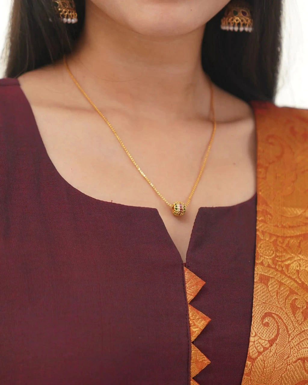 Gold necklace with a pendant worn by a person in a maroon and orange traditional outfit.
