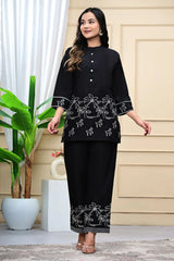 Woman wearing a black outfit with white embroidery in an outdoor setting.