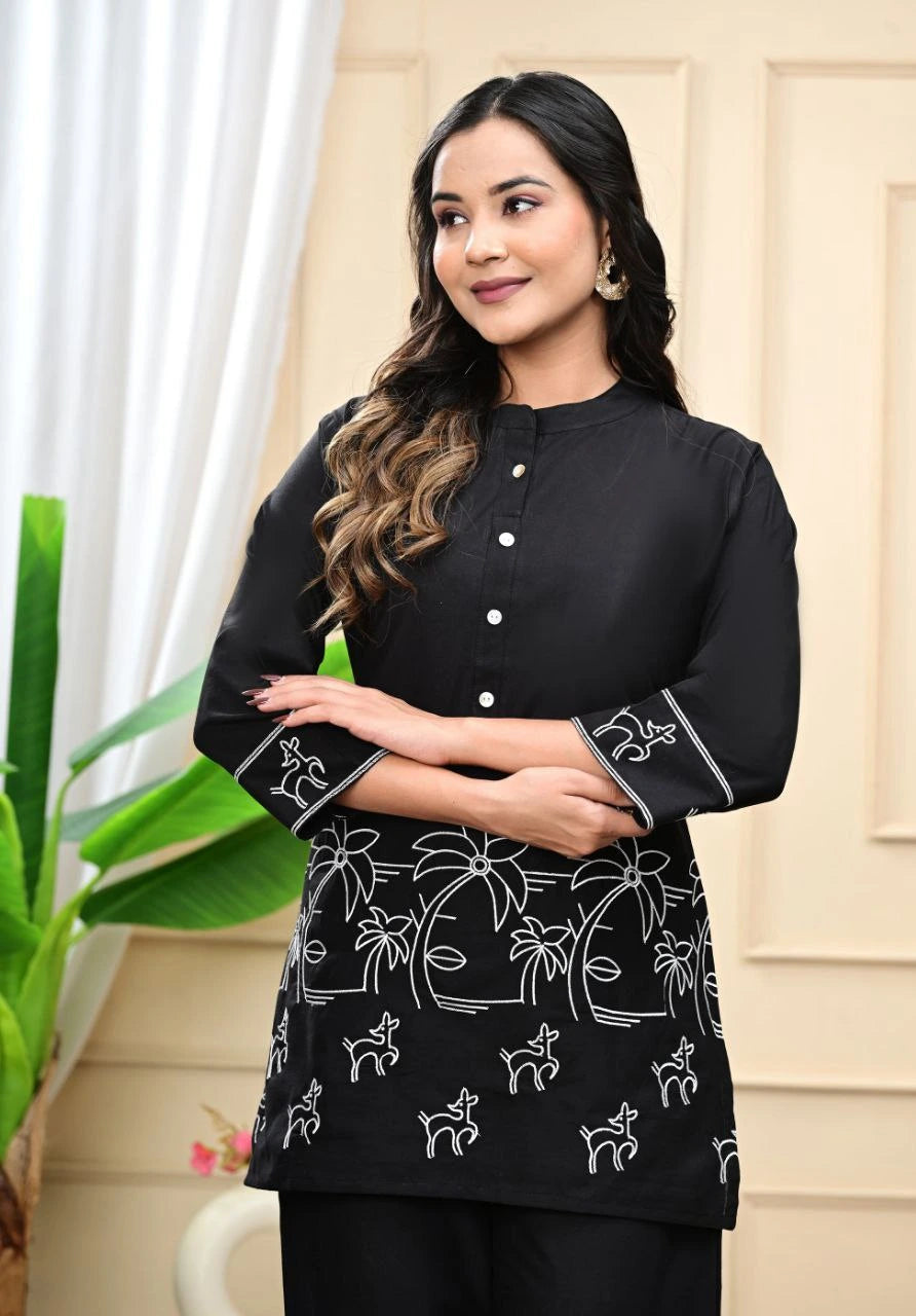 Woman wearing a black top with white patterns, standing indoors.