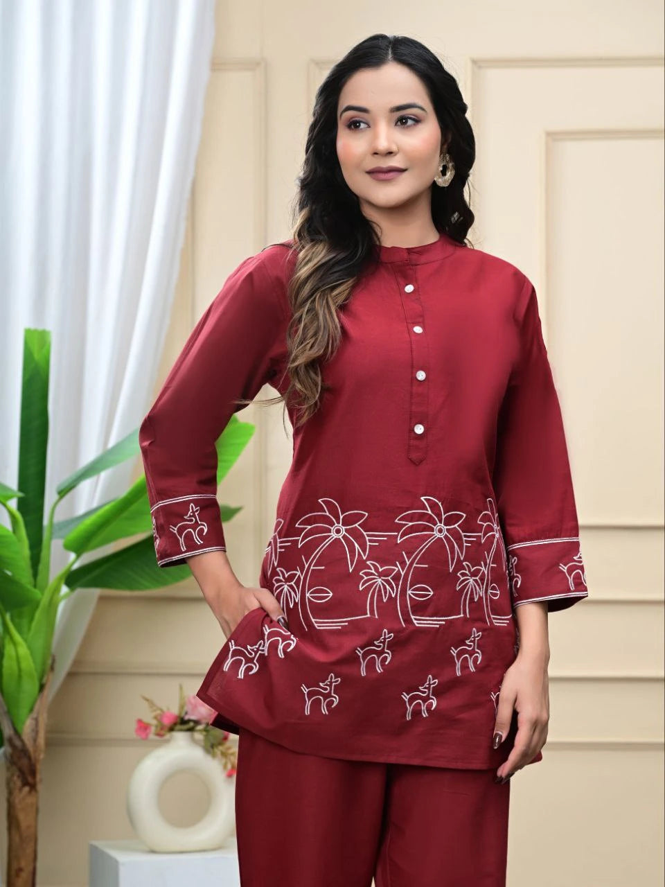 Woman wearing a maroon traditional outfit with white patterns in a home setting