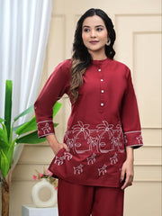 Woman wearing a maroon traditional outfit with white patterns in a home setting