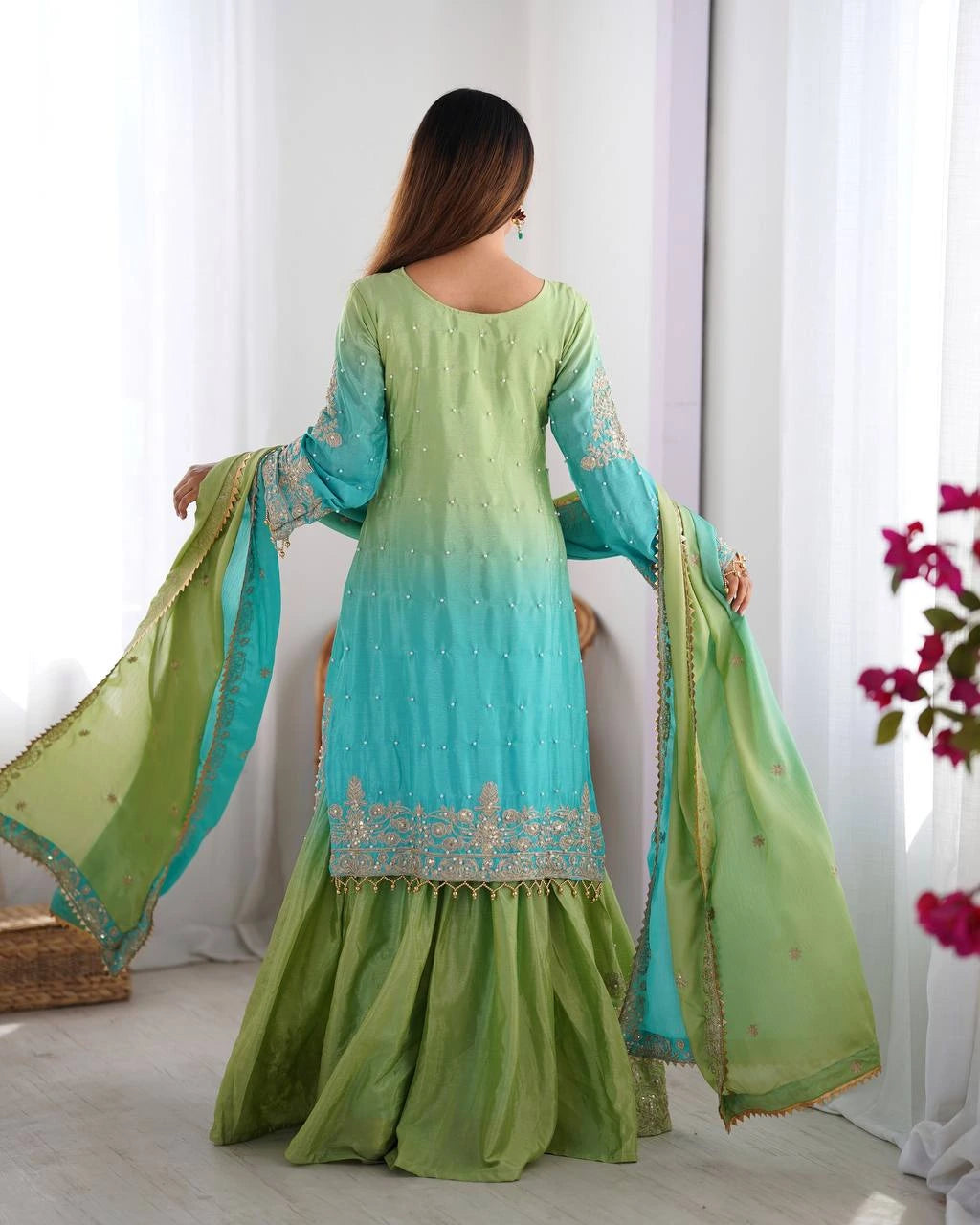 Woman wearing a green and blue traditional outfit with a matching dupatta in a bright room.