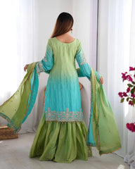 Woman wearing a green and blue traditional outfit with a matching dupatta in a bright room.