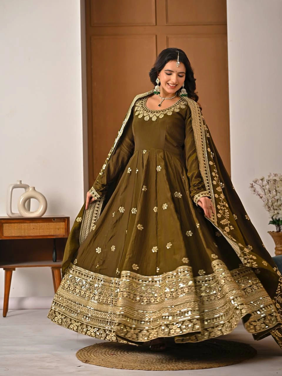 Woman wearing a traditional olive green dress with gold embroidery in a room setting.