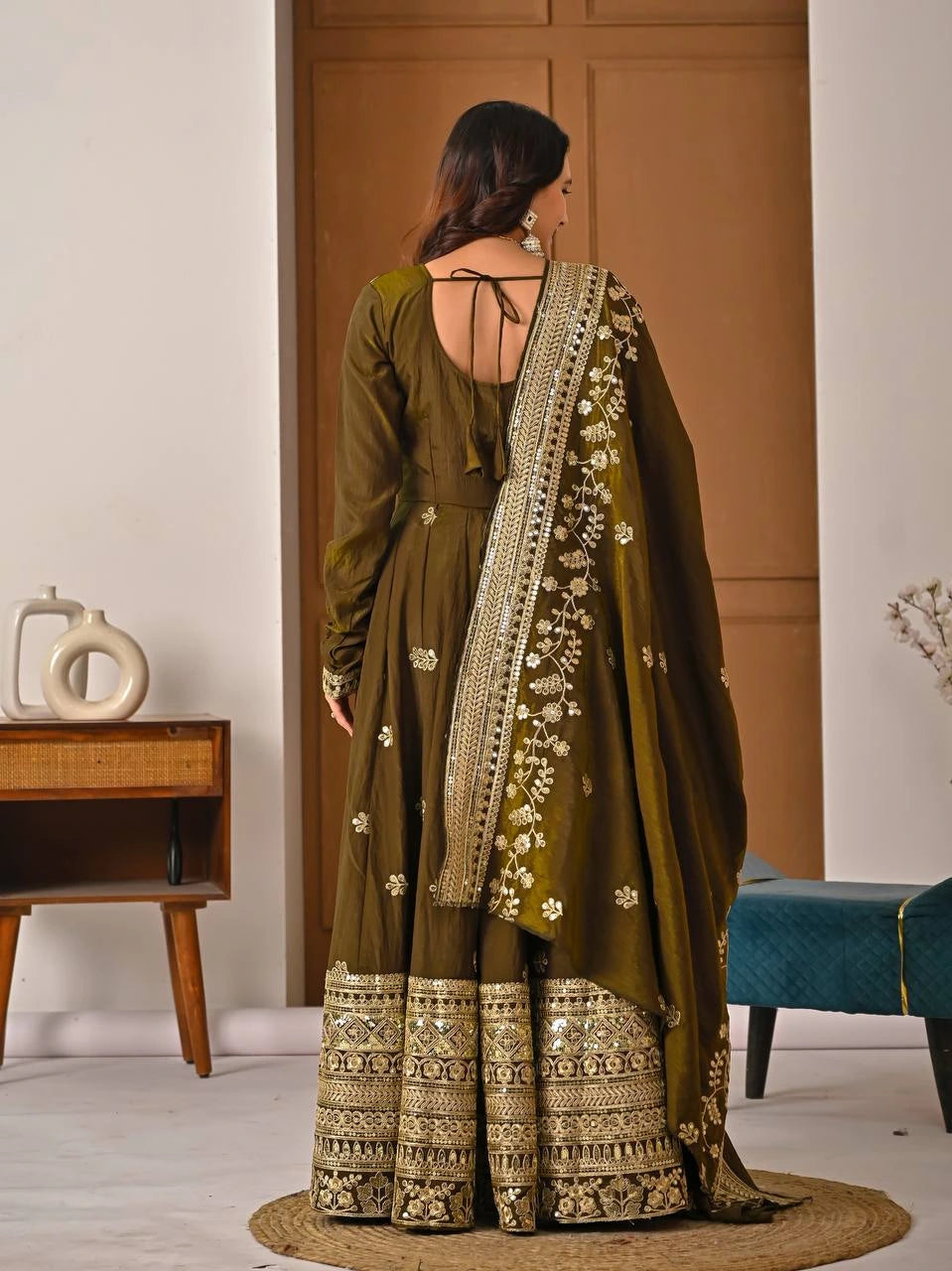 Woman in a traditional green and gold outfit with a matching dupatta in a room.