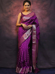 Woman wearing a purple saree with silver border against a dark background