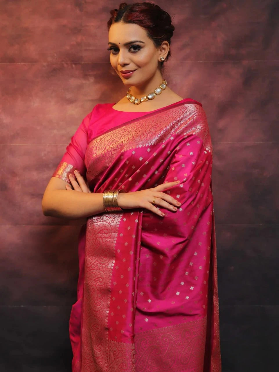 Woman wearing a pink saree with a gold border against a dark background