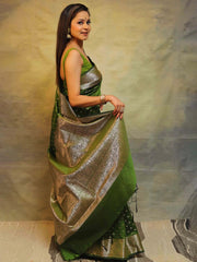 Woman wearing a green and gold saree against a neutral background