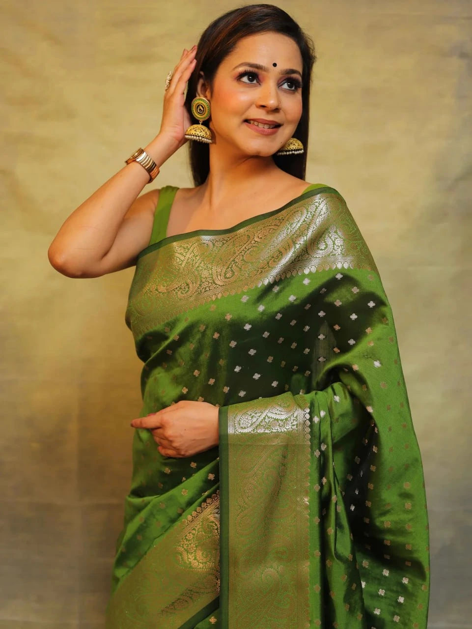 Woman wearing a green saree with a gold border against a beige background