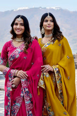 Two women in traditional pink and yellow sarees with mountainous background
