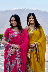 Two women in traditional sarees standing outdoors with a mountainous background.