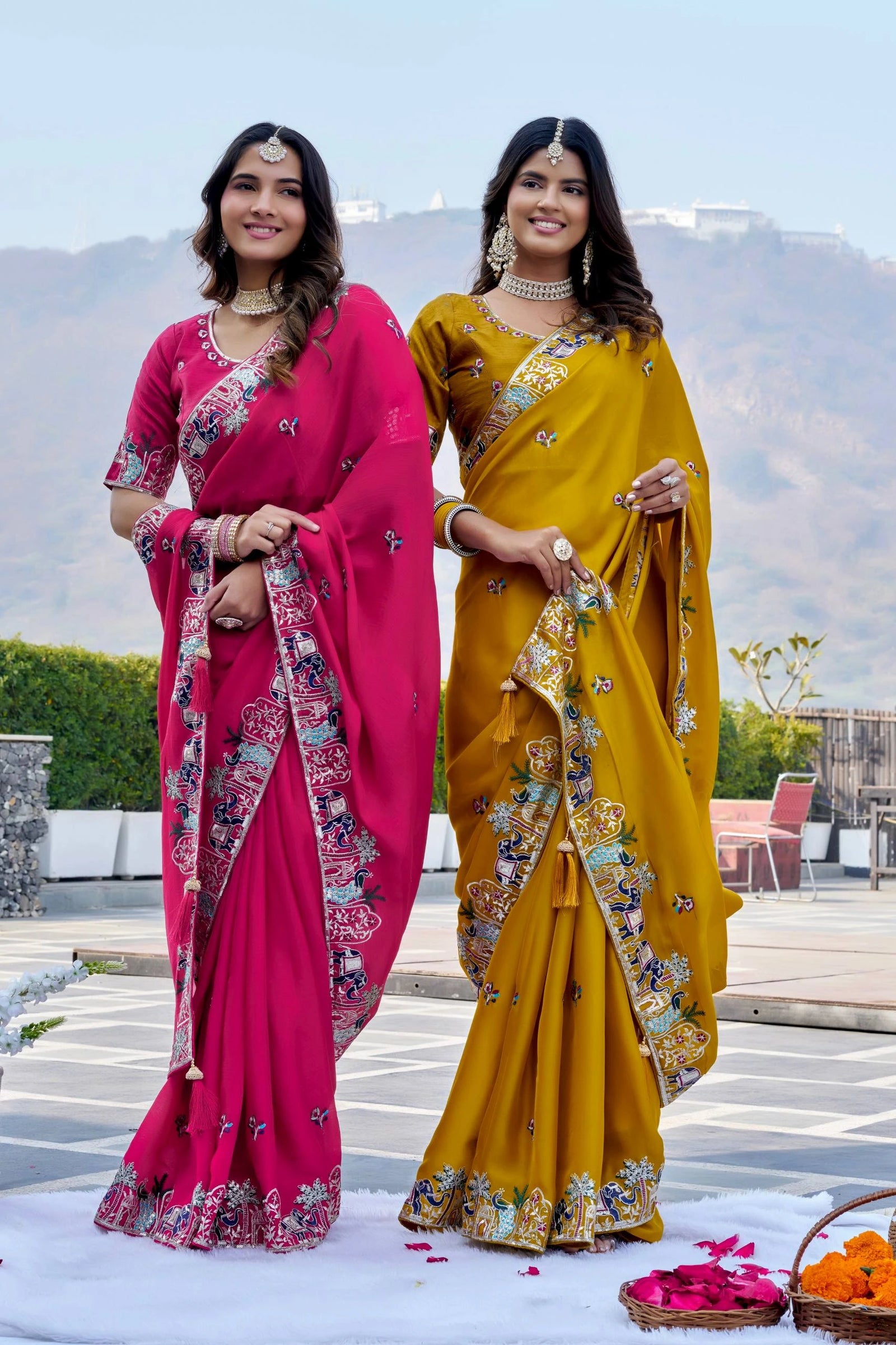 Two women in colorful sarees standing outdoors with a scenic background