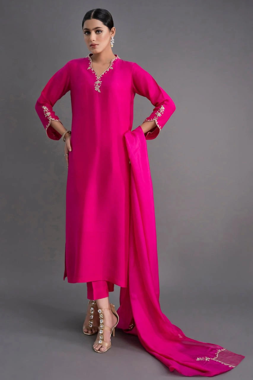 Woman wearing a bright pink traditional outfit with a long scarf on a gray background