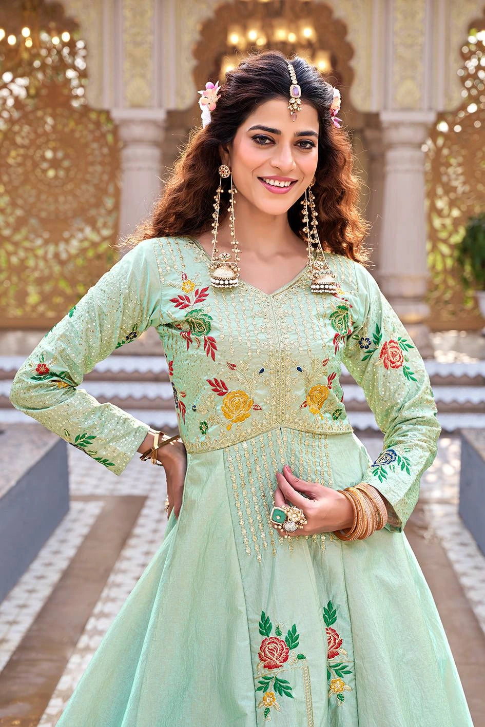 Woman wearing a light green embroidered traditional outfit with floral patterns in an indoor setting.
