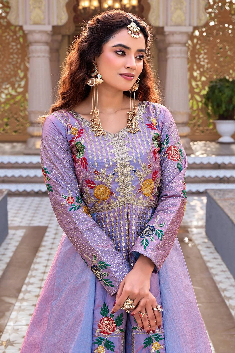 Woman in a traditional embroidered outfit standing in an ornate indoor setting.