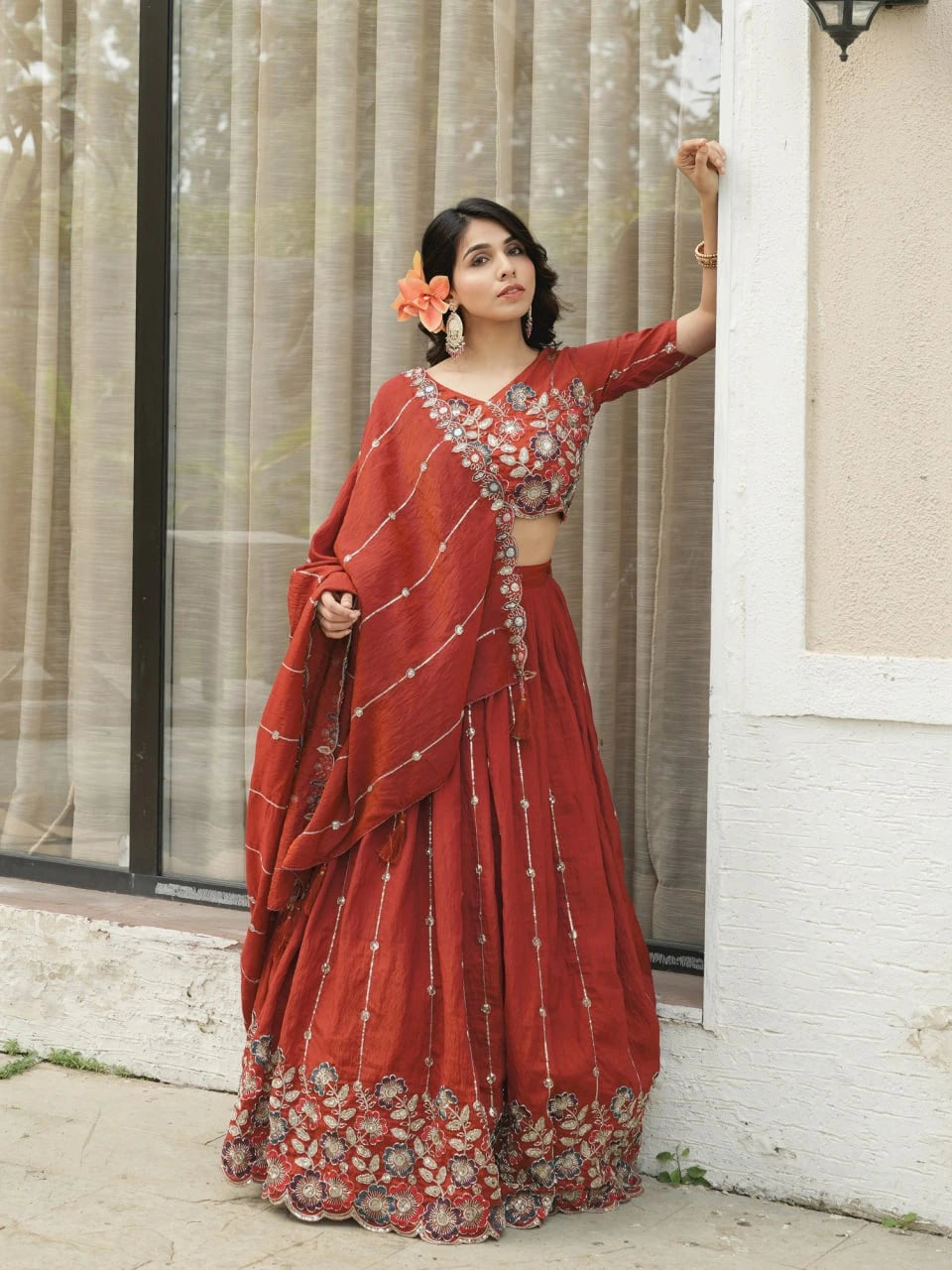 Woman in a red traditional outfit standing against a light-colored wall.