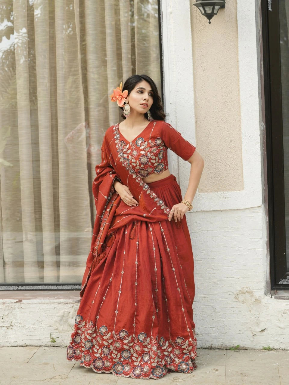 Woman in a red saree with floral design standing outdoors.