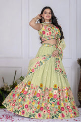 Woman wearing a floral green lehenga with a matching blouse against a white wall.