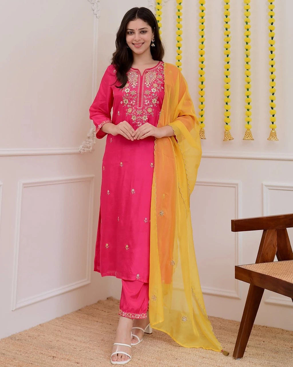 Woman wearing a pink and yellow traditional outfit in a room with decorative elements.