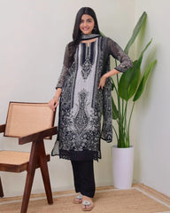 Woman wearing a black and white embroidered outfit in a room with a chair and plant.