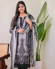 Woman wearing a black and white patterned dress with a scarf, standing indoors with a plant in the background.