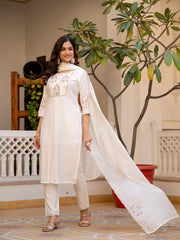 Woman in a white traditional outfit standing indoors with plants in the background