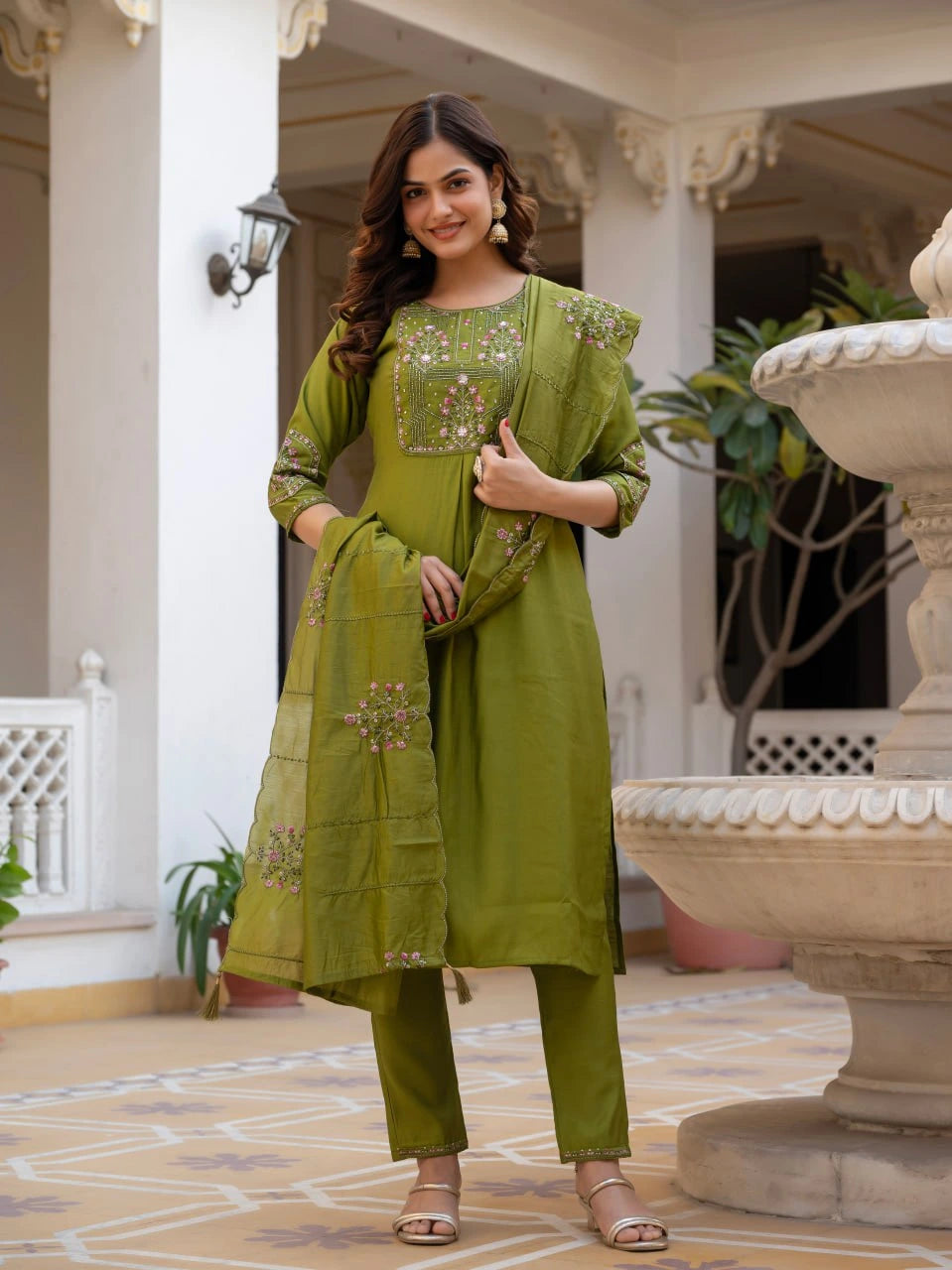 Woman in a green traditional outfit standing in an elegant indoor setting.