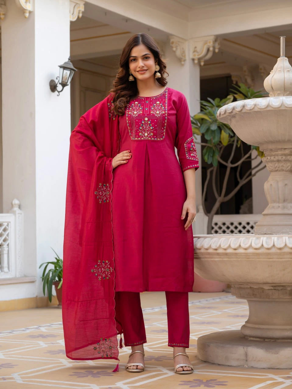 Woman in a red traditional outfit standing in an outdoor setting with decorative elements.
