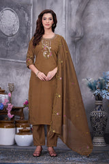 Woman wearing a brown traditional outfit with embroidery in a decorative setting.