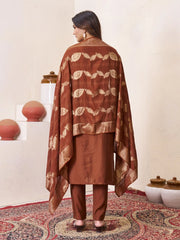 Woman wearing a brown traditional outfit with a patterned shawl in a decorative setting.