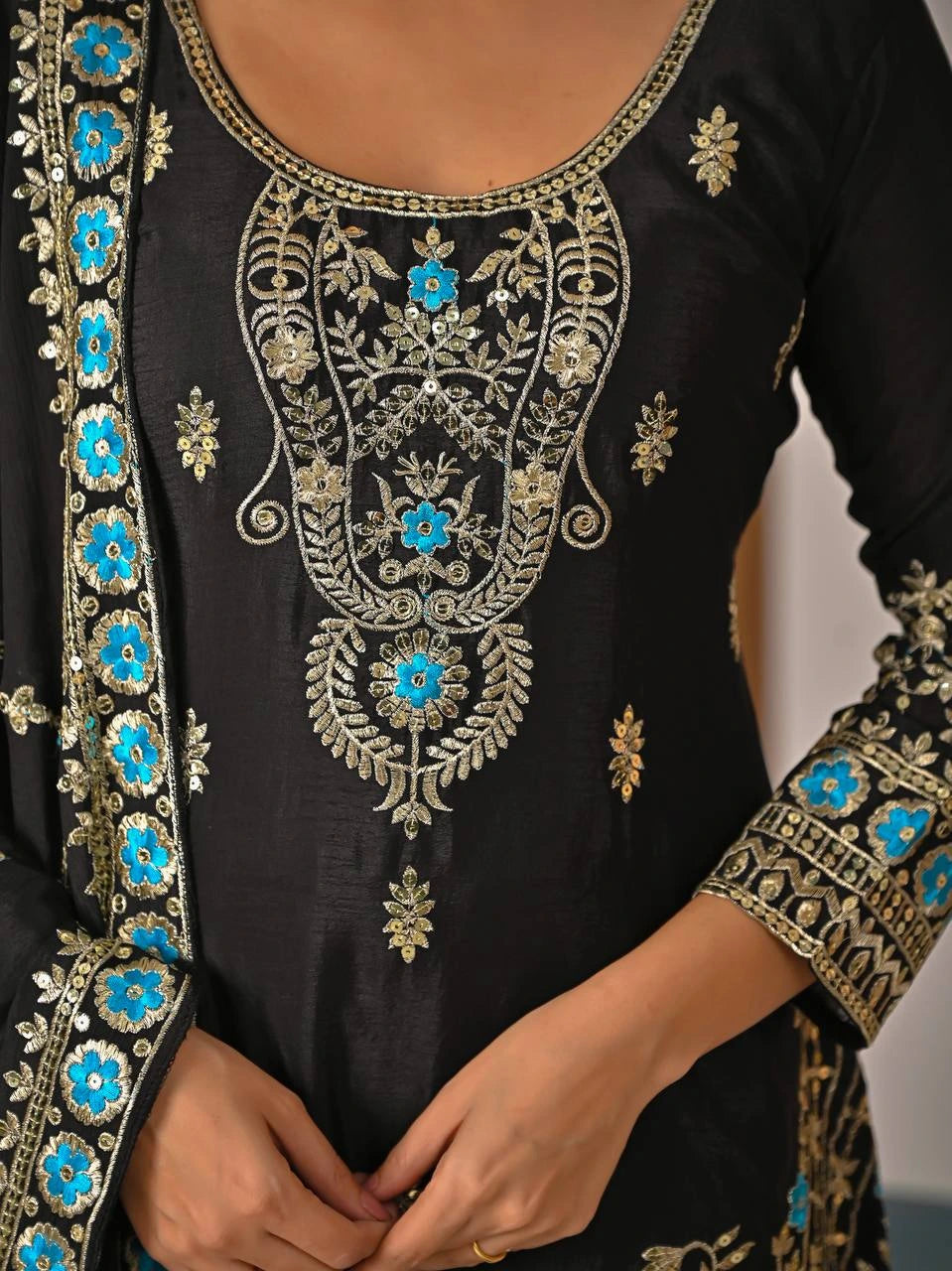 Black embroidered garment with blue floral patterns on a neutral background