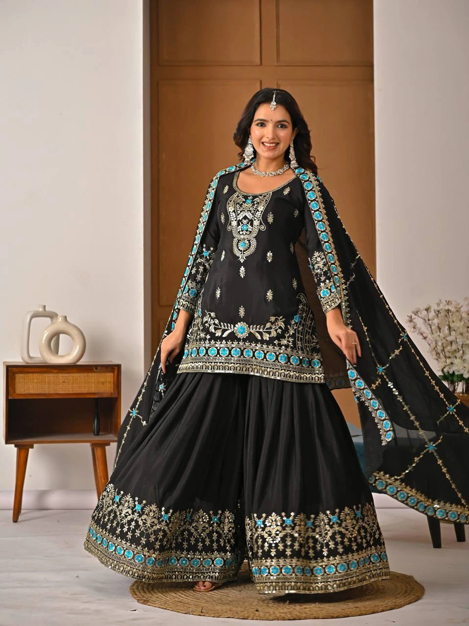 Woman wearing a black and blue embroidered traditional outfit indoors.