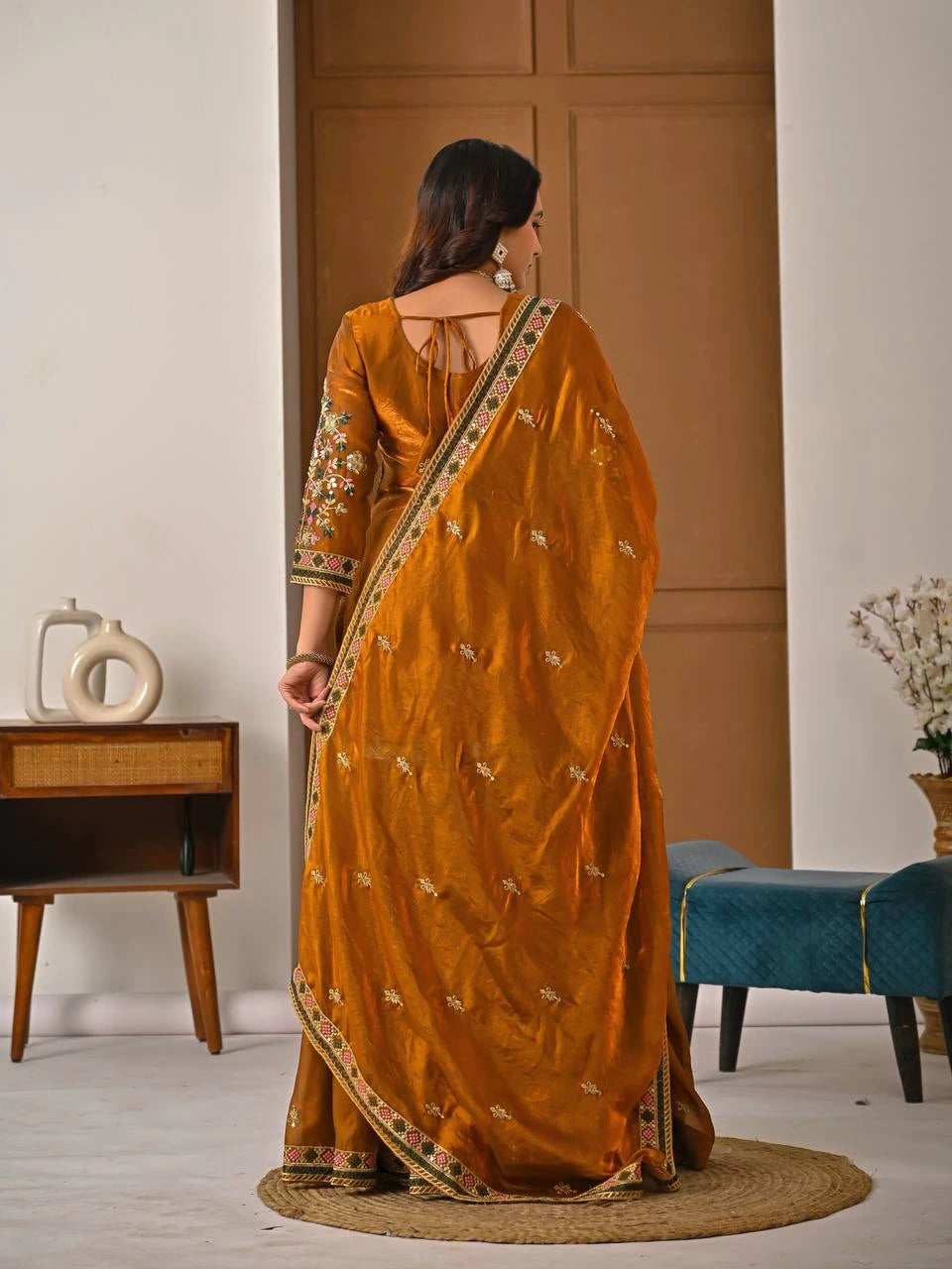 Woman in a mustard yellow saree with gold patterns standing in a room.