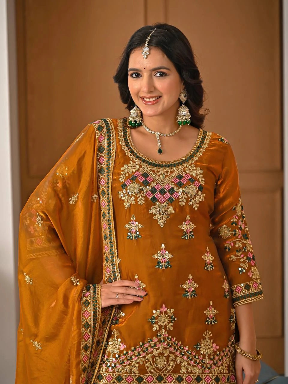 Woman wearing a traditional embroidered outfit with jewelry against a neutral background