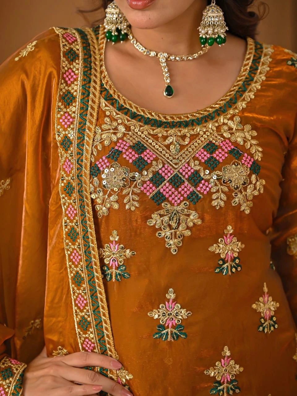 Close-up of a person wearing an orange embroidered outfit with jewelry.
