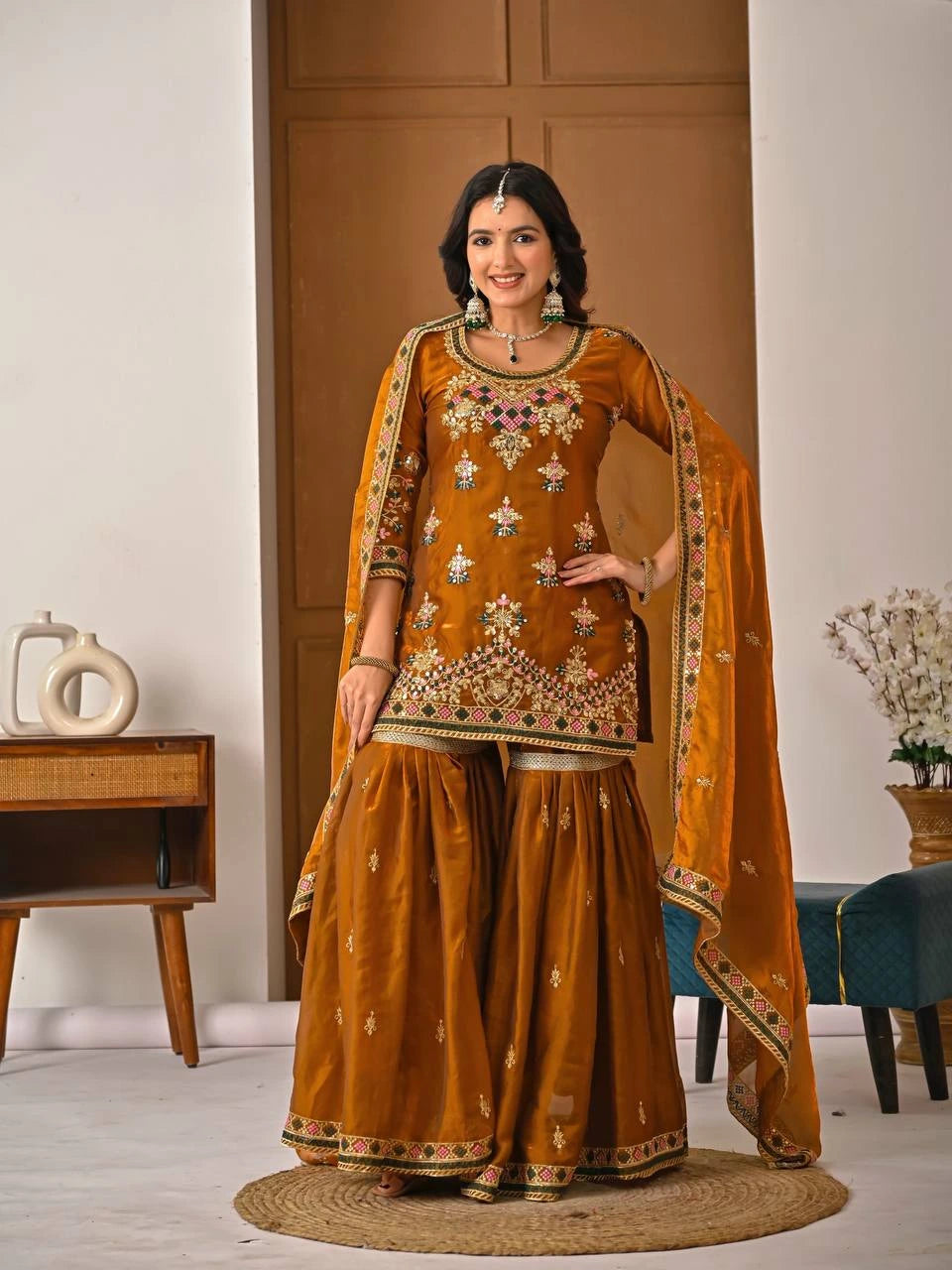 Woman in a mustard yellow embroidered traditional outfit standing indoors.