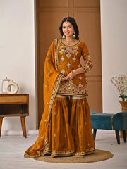 Woman in a traditional mustard yellow outfit with intricate patterns in a room setting.