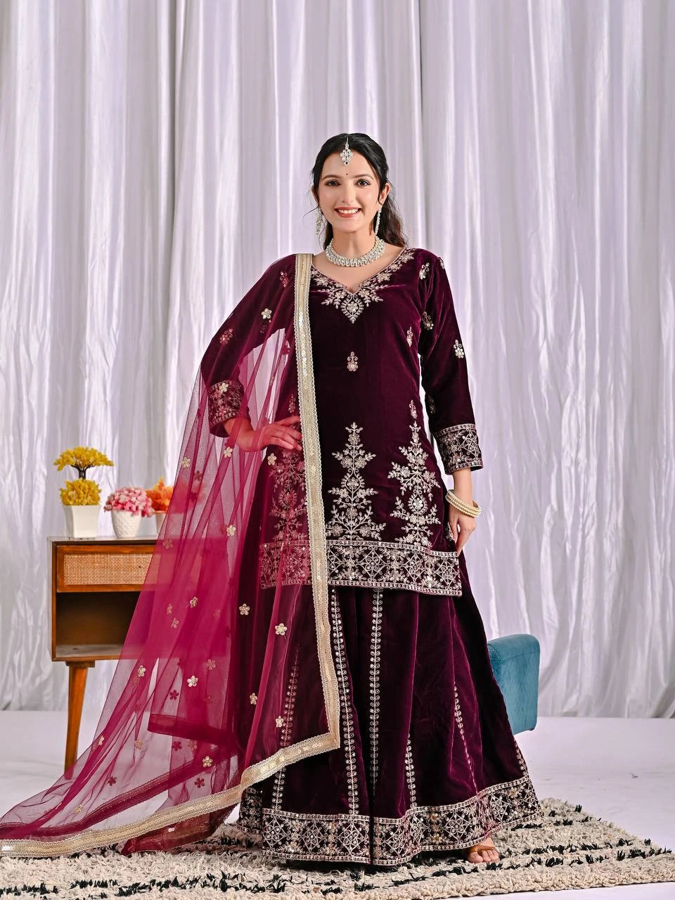Woman in a dark red traditional outfit with white embroidery against a white curtain background